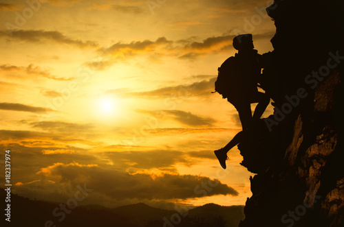 Silhouette of young woman lead climbing high.