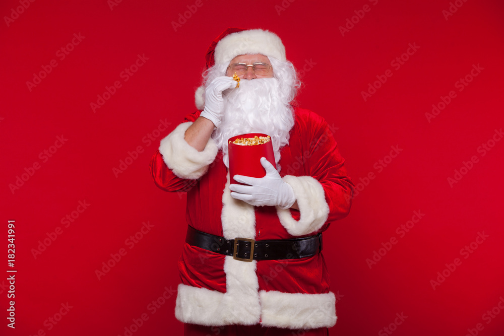 Traditional Santa Claus watching TV, eating popcorn. Christmas. Red background. emotions fear surprise Traditional Santa Claus watching TV, eating popcorn. Christmas. Red background. emotions fear surprise