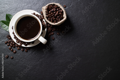 Top view mockup a cup of coffee with coffee beans and leaves on the black stone.