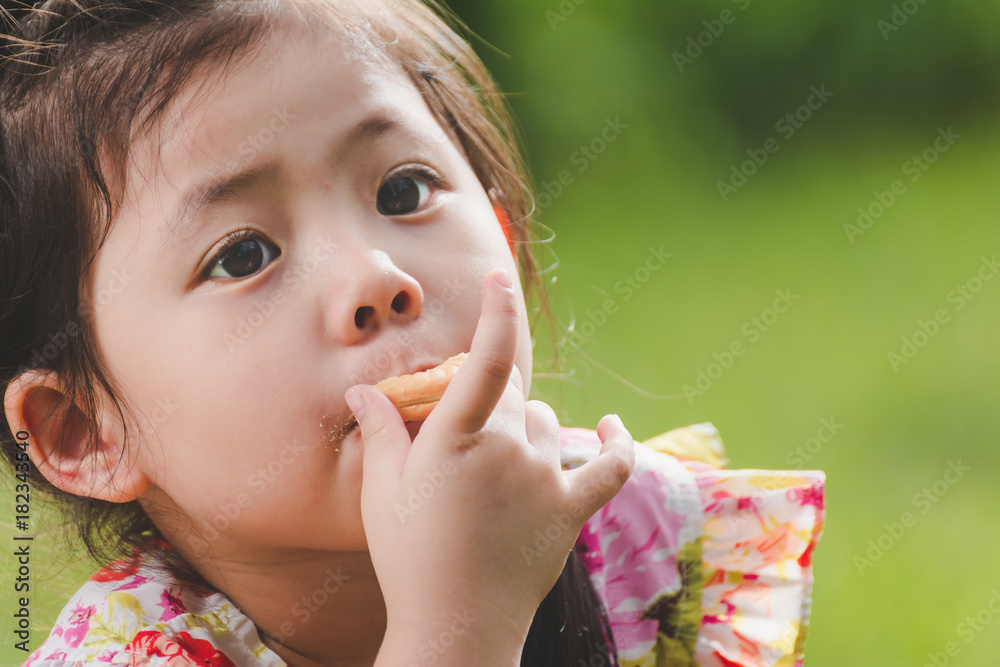 Portrait a Cute Little Asian Girl Eating cookie on Green Nature background. Portrait a Cute Little Asian Girl Eating cookie on Green Nature background.