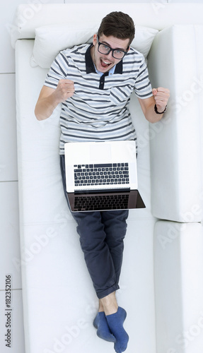 happy modern man looks at the laptop sitting on the couch.