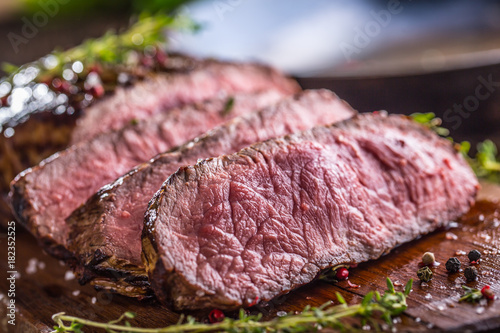 Beef steak. Juicy medium Rib Eye steak slices on wooden board with fork and knife herbs spices and salt