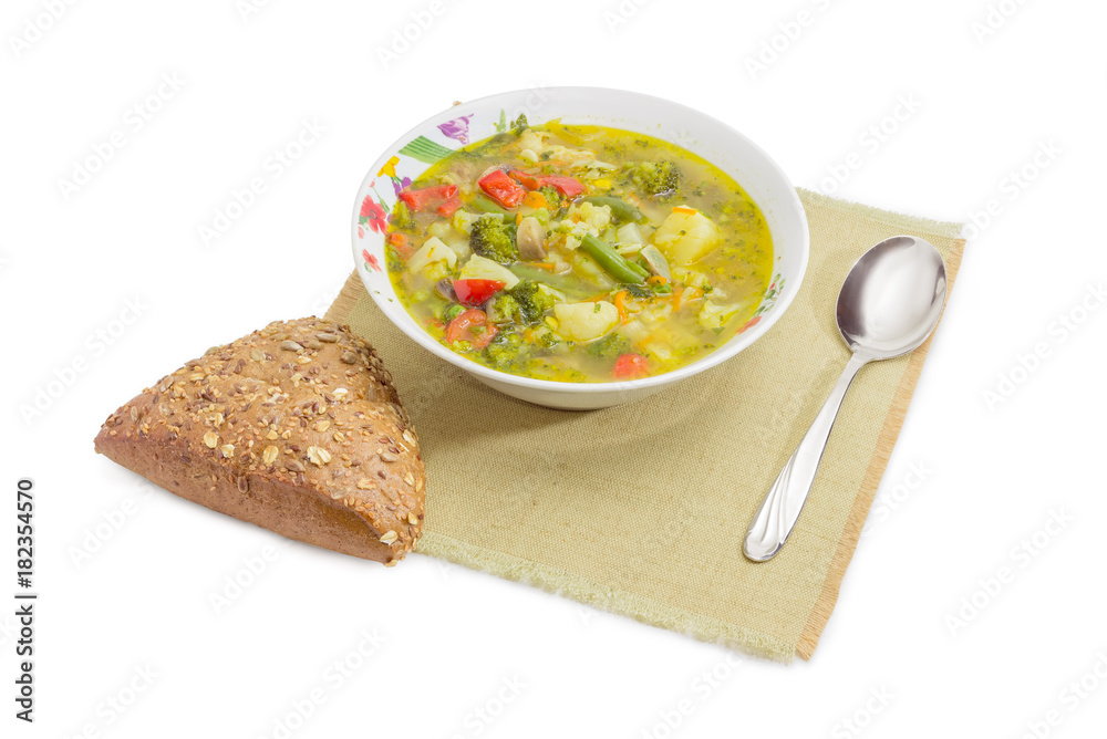 Bowl of vegetable soup, brown bread and spoon on napkin