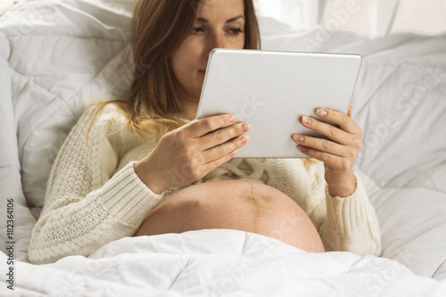 Pregnant young woman in bed with a tablet  reads information infants