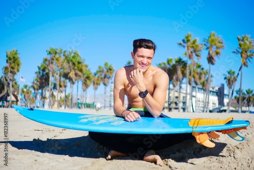 Handsome boy sit on the beach with surfboard, sunny day, California © Tatiana
