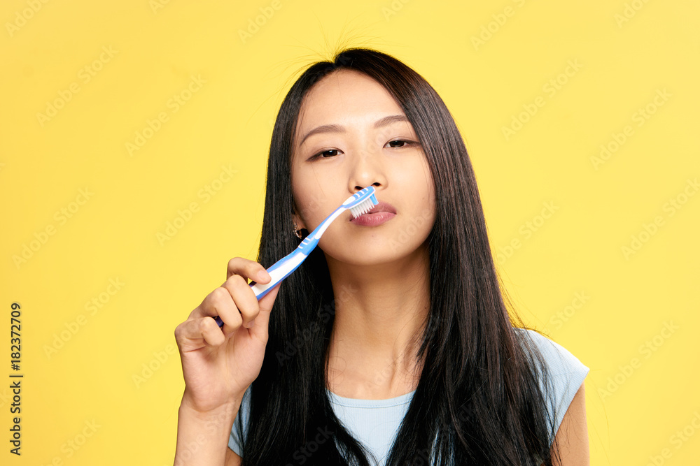 Young beautiful woman on a yellow background holds a toothbrush, Asian, portrait Young beautiful woman on a yellow background holds a toothbrush, Asian, portrait