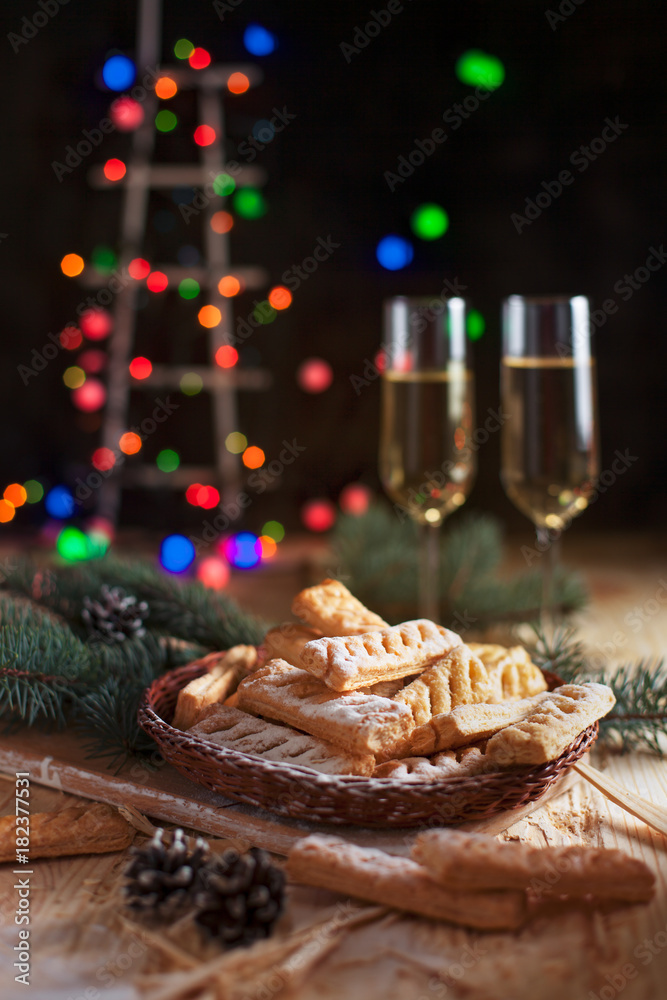 homemade cookies, glasses with champagne and a New Year tree on a festive table on a background of multi-colored New Year's lights