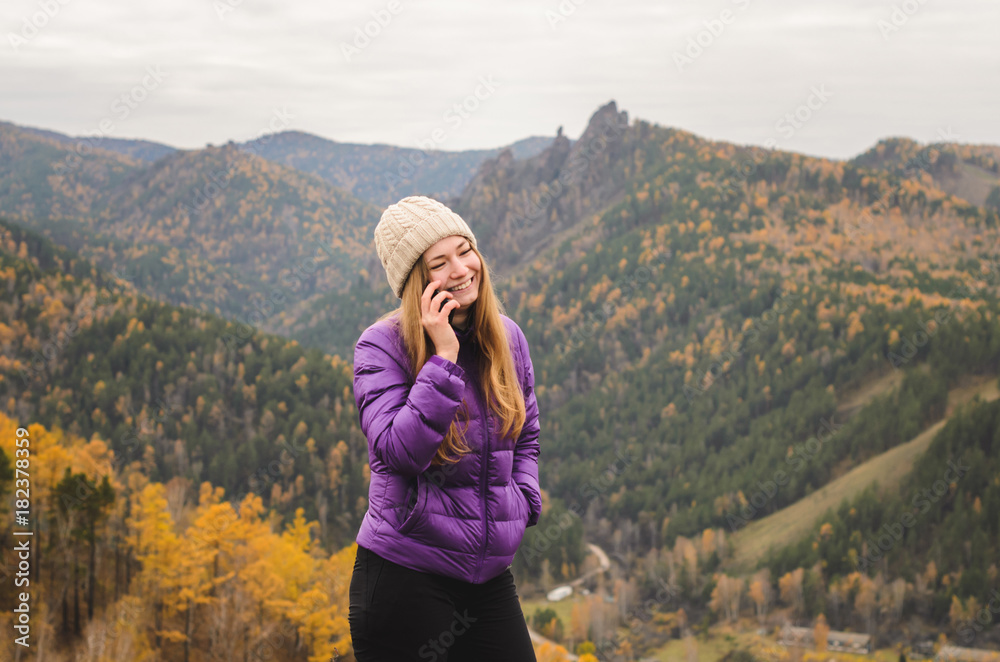 A girl in a lilac jacket talking on the phone in the mountains, an autumn forest with a cloudy day, free space for text