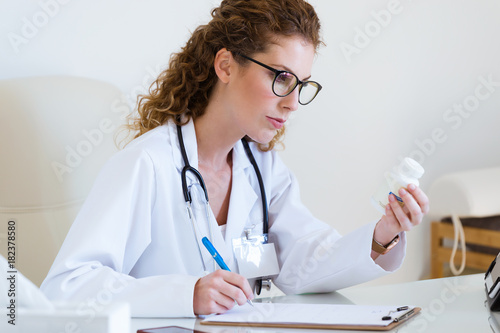 Beautiful female pharmacist holding jar of pills in hands in the office.