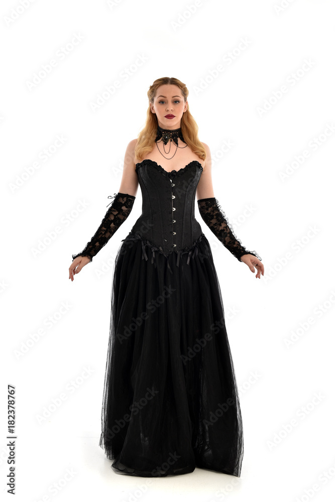 full length portrait of a blonde girl wearing black gothic gown. standing pose, isolated on white background.