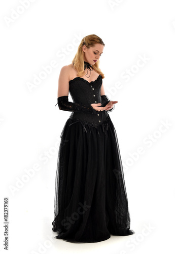 full length portrait of a blonde girl wearing black gothic gown. standing pose, isolated on white background.