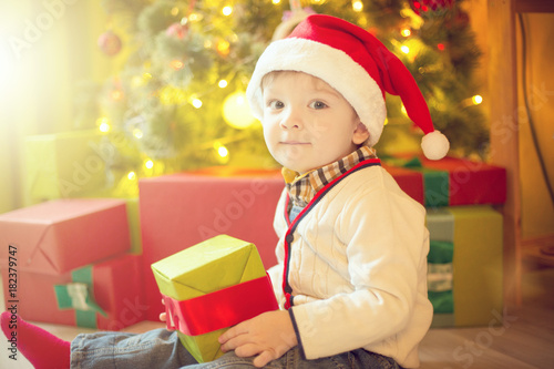 Happy little boy with Xmas present on Christmas Eve in decorated room. Sunny morning or day. Christmas or New Year holiday photo