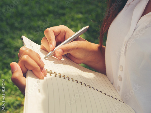Close up hand of young woman writing book at the park.