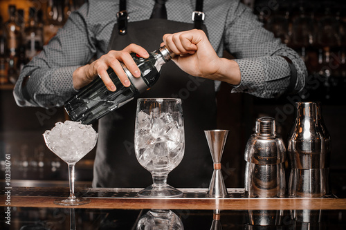 Barman in the apron making a cocktail with help of bar equipment photo