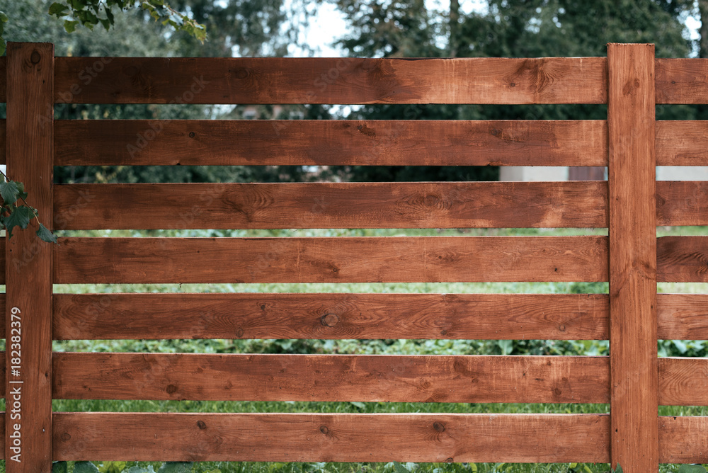 Wooden fence, a pen for horses, brown of boards. Green grass and trees against the background of boards. Summer autumn day in nature. Wooden fence, a pen for horses, brown of boards. Green grass and trees against the background of boards. Summer autumn day in nature.