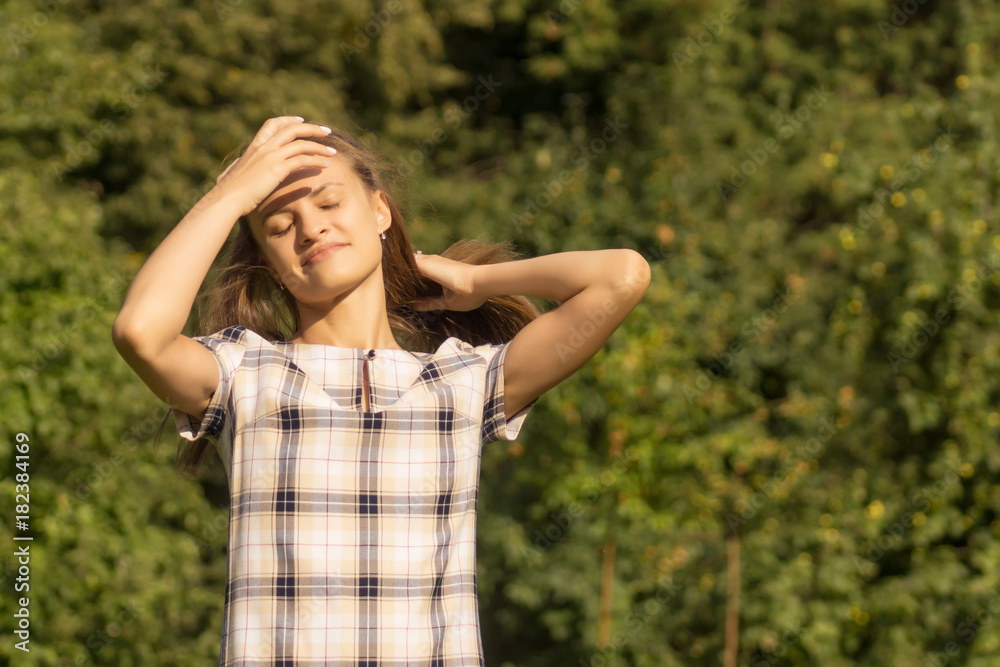 Portrait of a young beautiful woman adjusting her hair on a sunny day. Cute girl straightens her hair in the bright sun Portrait of a young beautiful woman adjusting her hair on a sunny day. Cute girl straightens her hair in the bright sun