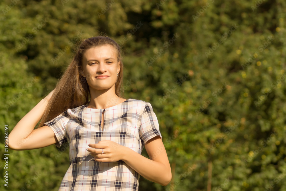 Portrait of a young beautiful woman adjusting her hair on a sunny day. Cute girl straightens her hair in the bright sun Portrait of a young beautiful woman adjusting her hair on a sunny day. Cute girl straightens her hair in the bright sun