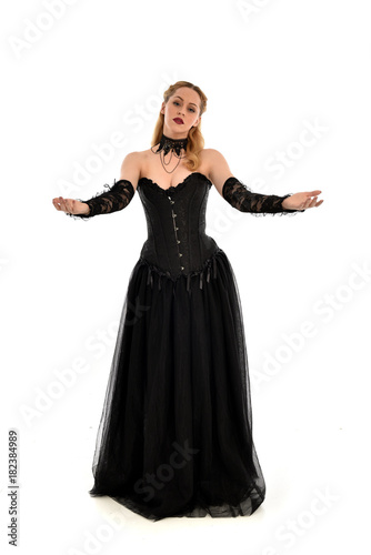 full length portrait of a blonde girl wearing black gothic gown. standing pose, isolated on white background.