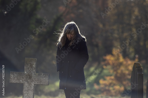 Mortality. Living with grief. Lady mourns at old cemetery grave on a cold autumnal morning. photo