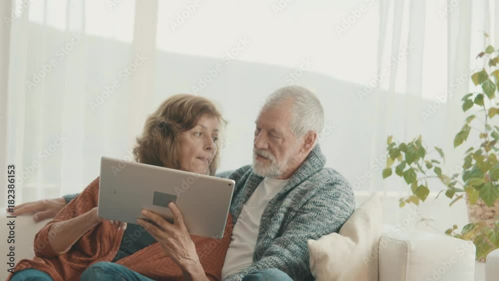 Senior couple with tablet relaxing at home.