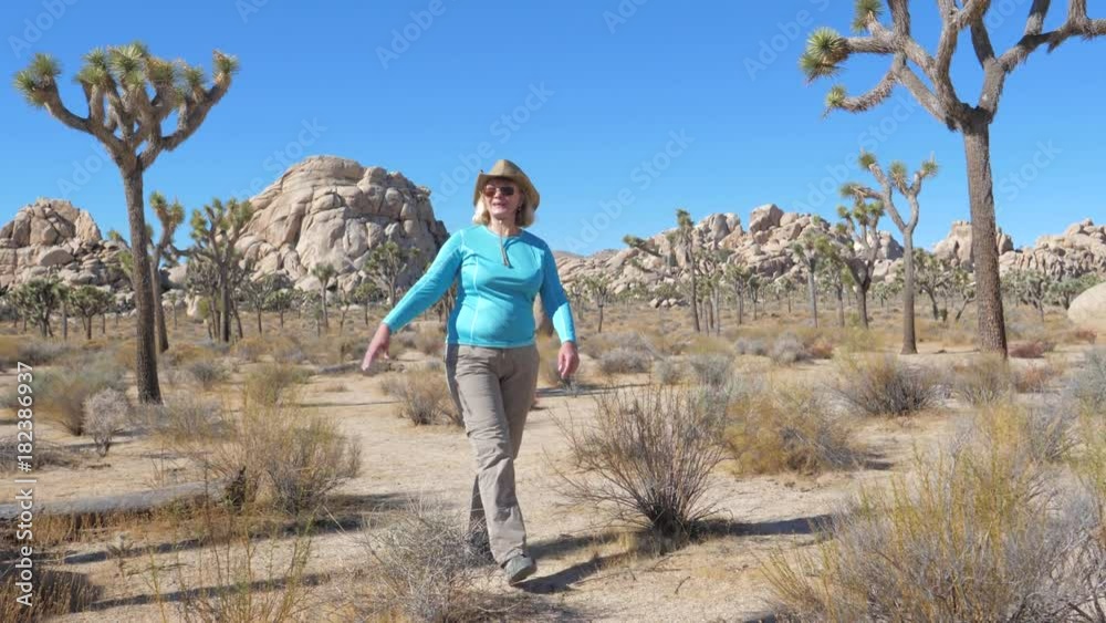 Woman In Cowboy Hat Walks Down The Middle Of The Mojave Desert, Waving Hand Woman In Cowboy Hat Walks Down The Middle Of The Mojave Desert, Waving Hand