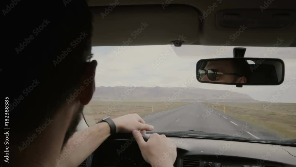 Back view of young man in sunglasses driving the vehicle, another man sitting near. Friends traveling together on car. Back view of young man in sunglasses driving the vehicle, another man sitting near. Friends traveling together on car.