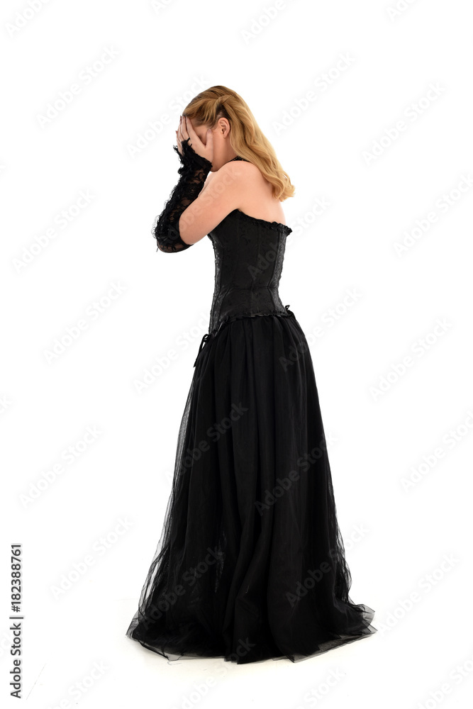 full length portrait of a blonde girl wearing black gothic gown. standing pose, isolated on white background.