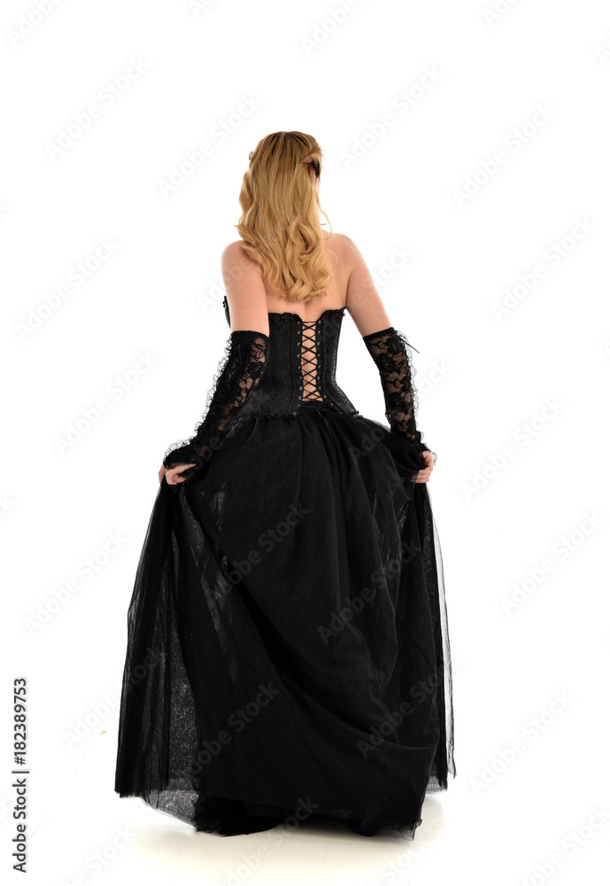 full length portrait of a blonde girl wearing black gothic gown. standing pose, isolated on white background.