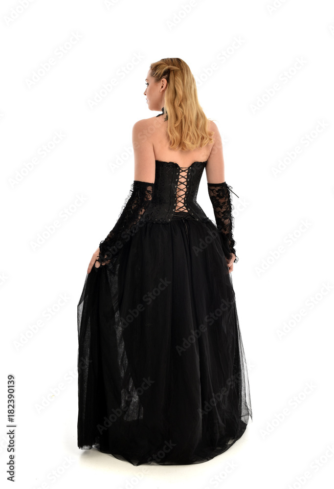 full length portrait of a blonde girl wearing black gothic gown. standing pose, isolated on white background.