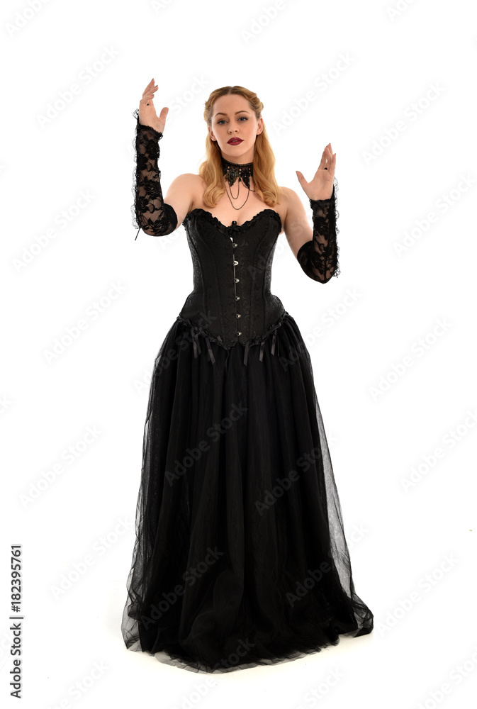full length portrait of a blonde girl wearing black gothic gown. standing pose, isolated on white background.