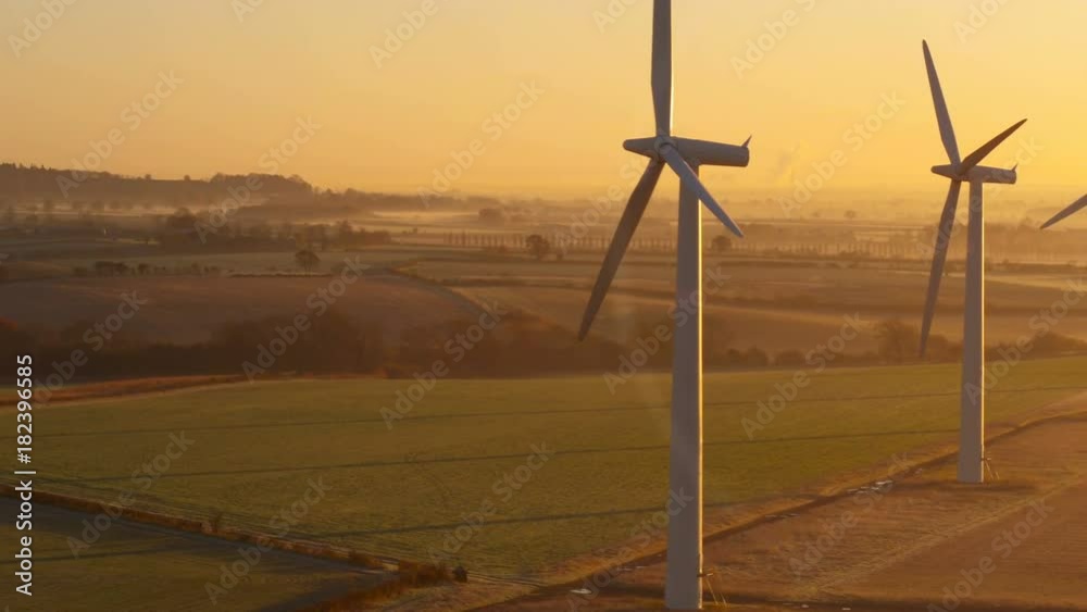 Slowly panning across five wind turbines from the air at sunrise on a very still day