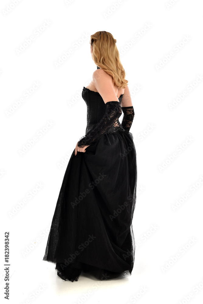 full length portrait of a blonde girl wearing black gothic gown. standing pose, isolated on white background.