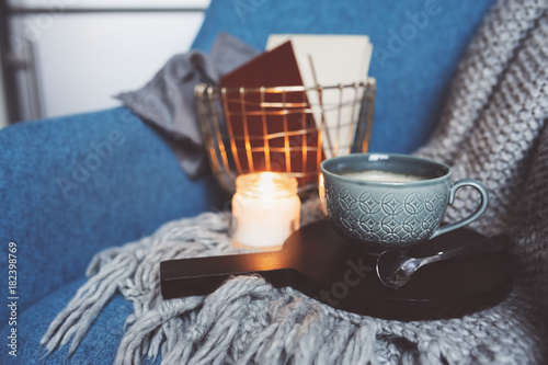 Cozy winter weekend at home. Morning with coffee or cocoa, books, warm knitted blanket and nordic style chair. Hygge concept.