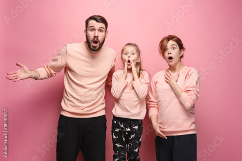Surprised young family looking at camera on pink