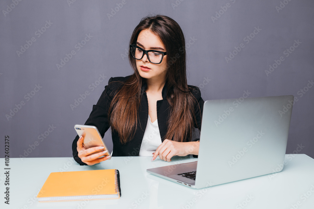Young smiling business woman using smartphone near computer in office Young smiling business woman using smartphone near computer in office