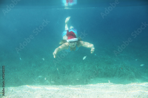 Woman in Santa hat swimming underwater