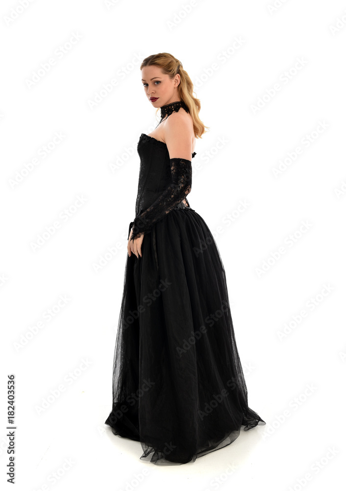 full length portrait of a blonde girl wearing black gothic gown. standing pose, isolated on white background.