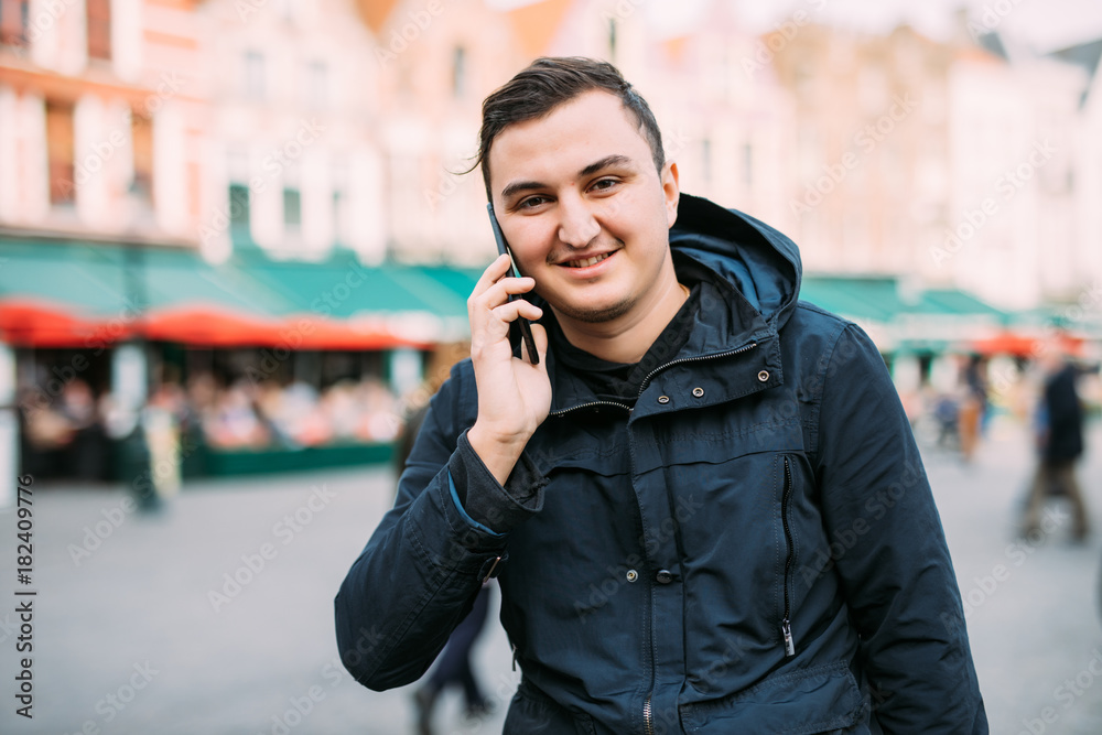 Front view of a happy man calling on the phone walking on the street Front view of a happy man calling on the phone walking on the street