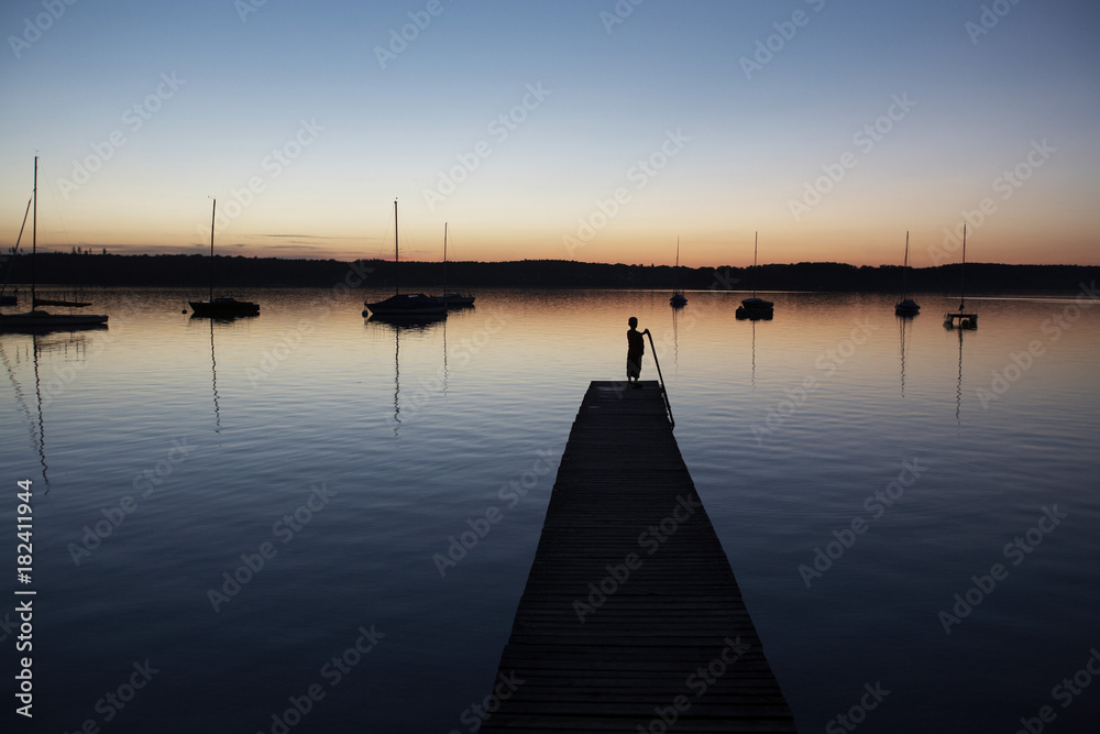 Silhouette of child at the end of jetty on lake at sunset, Germany Silhouette of child at the end of jetty on lake at sunset, Germany