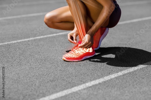 Low section of sportswoman tying shoelace on track