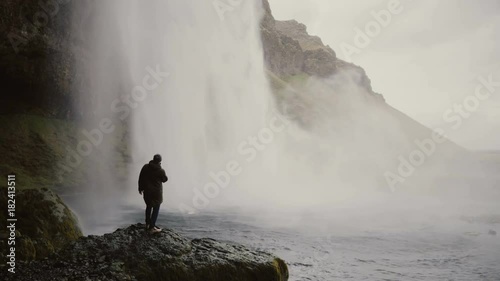 Young tourists with action camera near the Gljufrabui waterfall in Iceland. Man looking on famous sight of North nature.