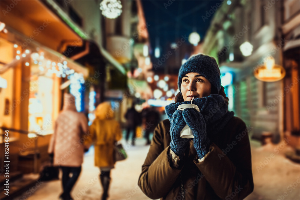 Pretty girl with coffee outdoor in cold weather with christmas lights behind Pretty girl with coffee outdoor in cold weather with christmas lights behind