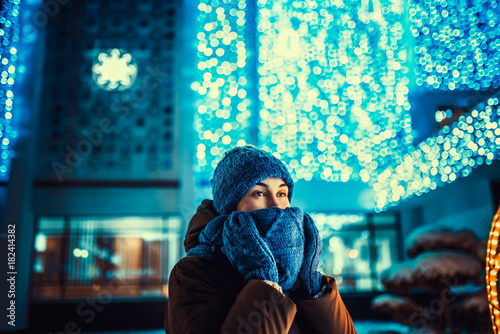 Pretty girl outdoor in cold weather with christmas lights behind © bedya