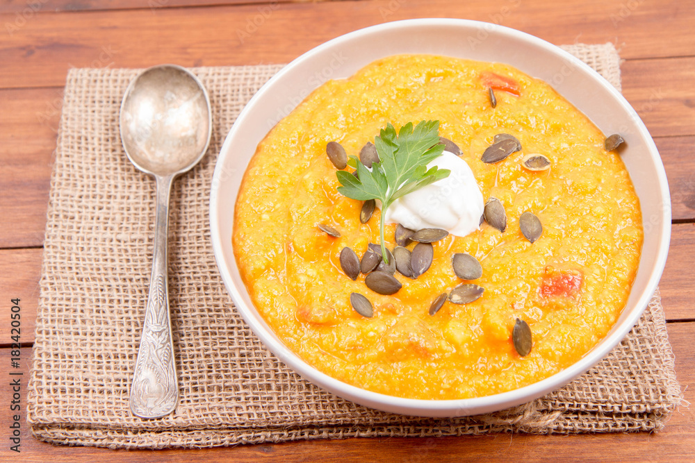 Pumpkin and carrot soup decorated with cream, parsley and pumpkin seeds on a wooden background