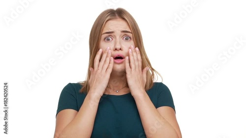 Closeup portrait of young scared woman 20s expressing fright being shocked hearing bad news raising hands to cheeks in fear over white background in slow motion. Concept of emotions