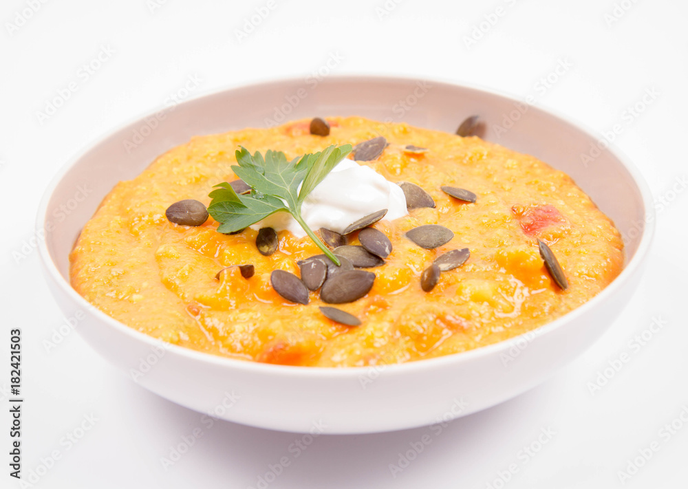 Pumpkin and carrot soup decorated with cream, parsley and pumpkin seeds on a white background Pumpkin and carrot soup decorated with cream, parsley and pumpkin seeds on a white background