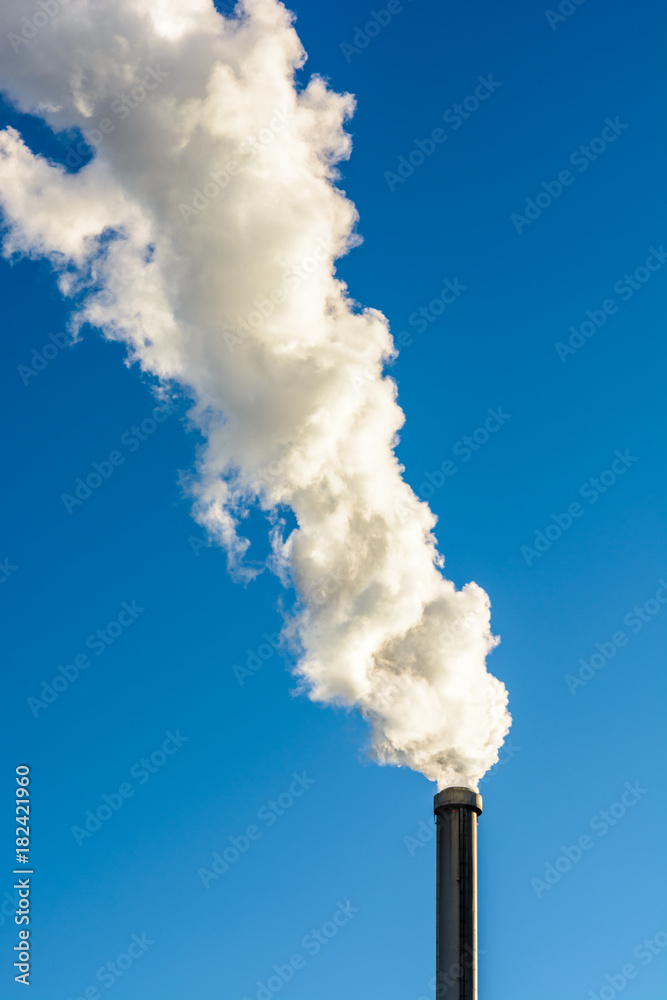 A long cloud of white smoke getting out of a metallic chimney against a deep blue sky. A long cloud of white smoke getting out of a metallic chimney against a deep blue sky.