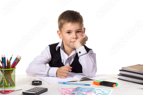 Cute intelligent pupil sitting at the desk with hand under the chin surrounded with stationery photo