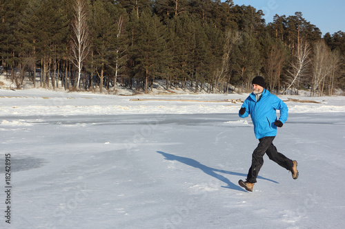 Man in a blue jacket running across the ice of a frozen river, Ob Reservoir, Russia