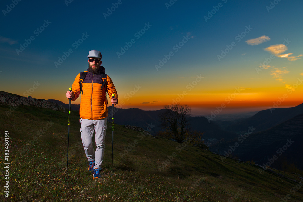 Young man with beard practicing nordic walking in a colorful sunset
